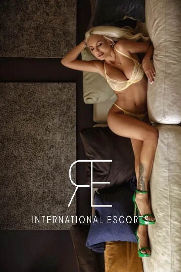 A picture of a busty blonde London escort laying down on a sofa in underwear and heels 