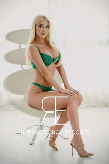 Blonde escort sitting in a chair wearing green lace lingerie 