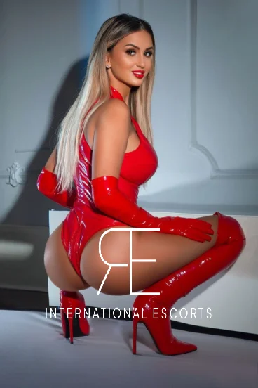 Kelly is crouching down and is wearing her red PVC outfit 