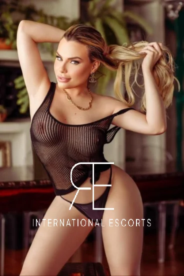 A very curvy blonde busty escort is wearing a black mesh top 