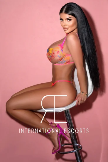 A busty London escort sitting on a stool wearing sexy underwear 