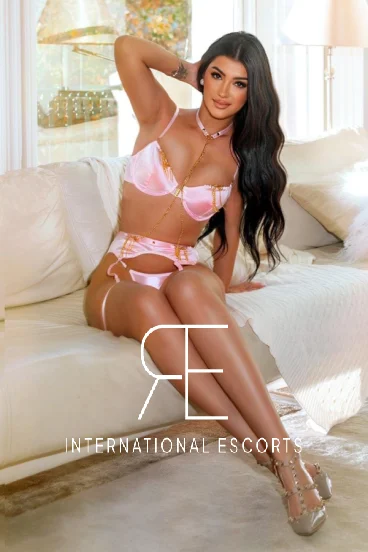 A very sexy brunette escort wearing pink underwear is sitting on a sofa 