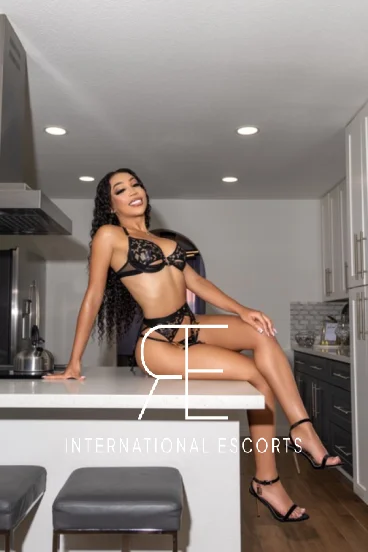 A very sexy ebony escort is sitting on her kitchen worktop 