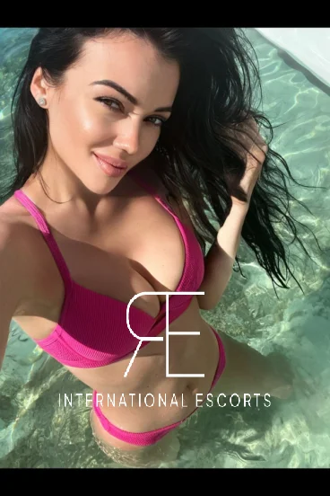 A selfie of a brunette lady in a pool wearing a pink bikini 