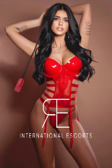 A beautiful brunette lady pictured wearing a red latex body and holding a whip 