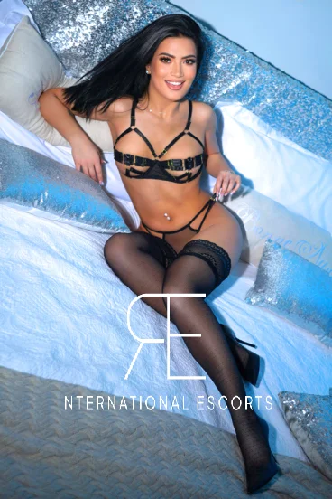 Sitting on a bed wearing some very sexy underwear is Bella-Bell a brunette London escort 
