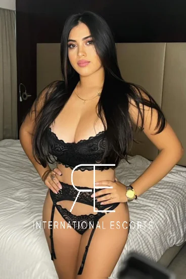 Busty London escort Emilia is standing by her bed 