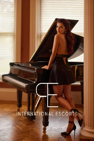 In this photo Rosie is standing by a piano and the London escort is wearing a black dress 