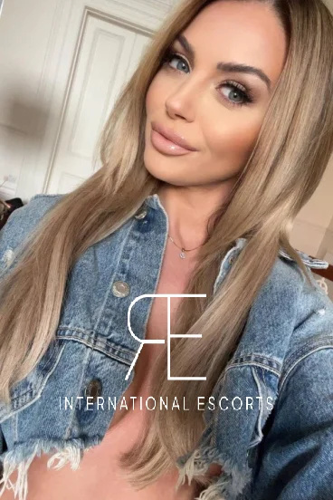 A very sexy young blonde escort has taken a selfie of herself wearing a jean jacket 
