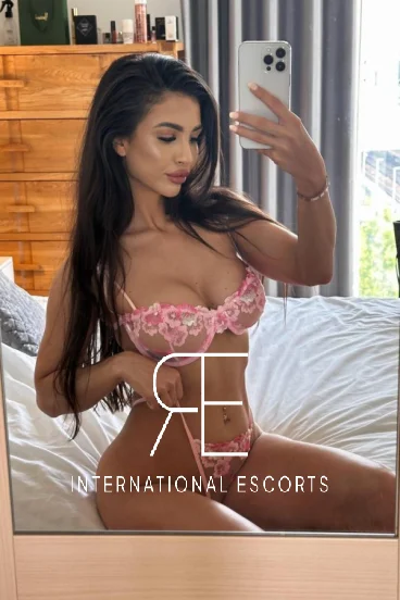 A very sexy brunette lady taking a lingerie selfie sitting on her bed 
