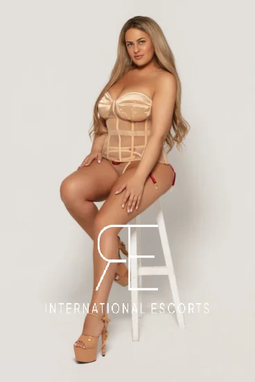 Blonde lady with large boobs sitting on a stool 