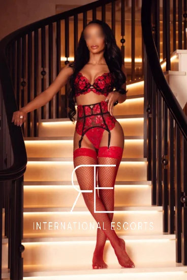 Asha a sexy Brazilian ebony escort in London is standing on a large stair case 