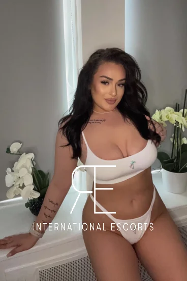 A very busty brunette escort wearing white sports lingerie 