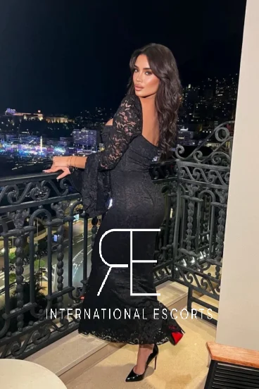 A vision of class, Tornia stands poised in black lace on a balcony above a glittering skyline.