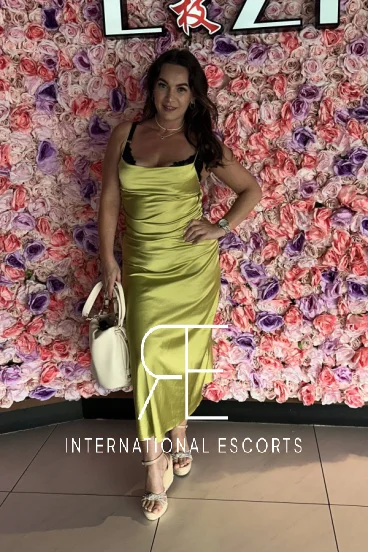 Elegant Lucy Rose in a silky gold dress, photographed against a floral backdrop 