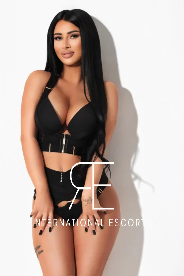 Beautiful brunette London escort in black lingerie, confident pose