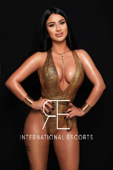 Brunette London escort in gold plunge swimsuit and bangles