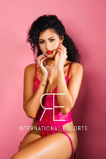 Gigi, ebony beauty in red lingerie and pearls against pink wall