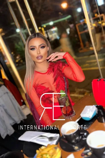 Stylish brunette London escort in luxury red dress at chic restaurant 