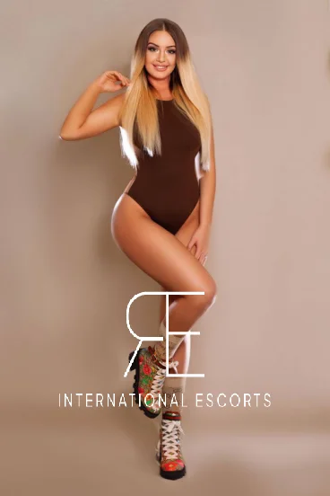 Cosmopolitan blonde Caprice in fitted brown bodysuit and couture boots