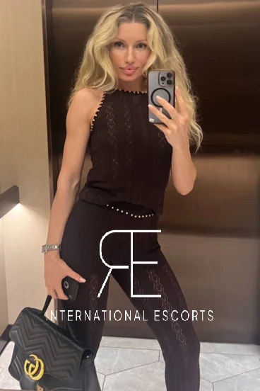 Cosmopolitan Zenadia blonde escort in chic black outfit, poised traveller