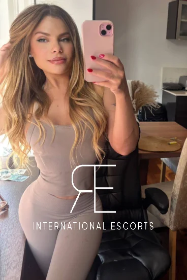 Slim blonde escort wearing a beige jumpsuit 