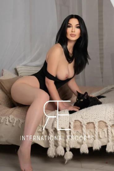 Rosaline reclining on bed, cosmopolitan escort in black one-piece