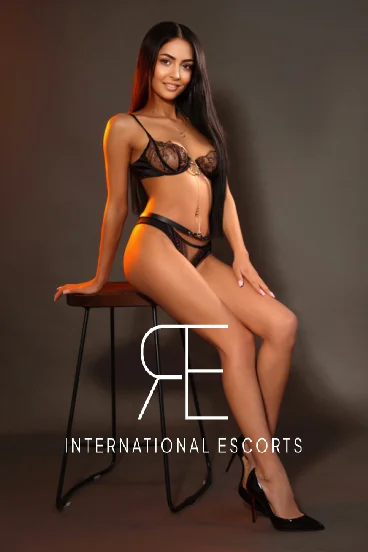 Slim figure in black lace set, perched elegantly on a stool.