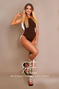 Cosmopolitan blonde Caprice in fitted brown bodysuit and couture boots