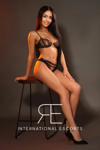 Slim figure in black lace set, perched elegantly on a stool.